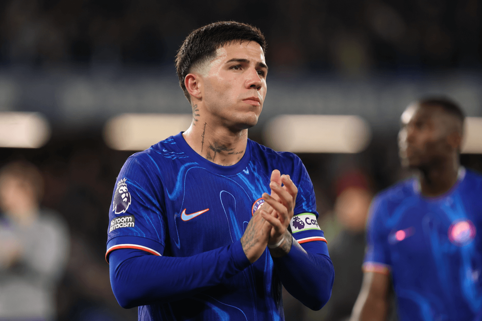 Enzo Fernández-style midfielder in blue kit applauding supporters after a match amid Chelsea transfer uncertainty